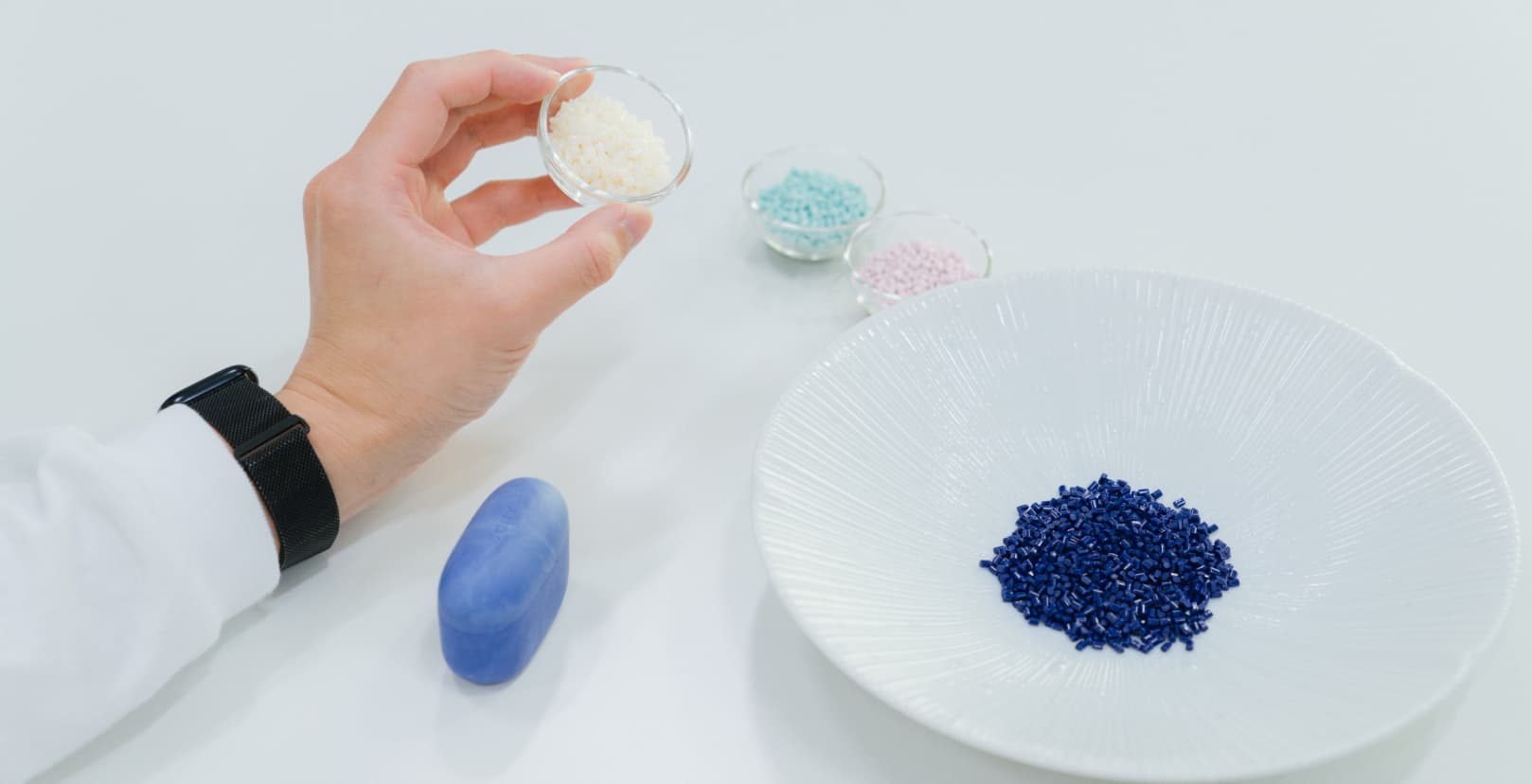 本坊健一郎さんが透明の素材を持っている手のアップとLink Buds S、ピンク、ブルー、ブルーのマーブルの素材の写真