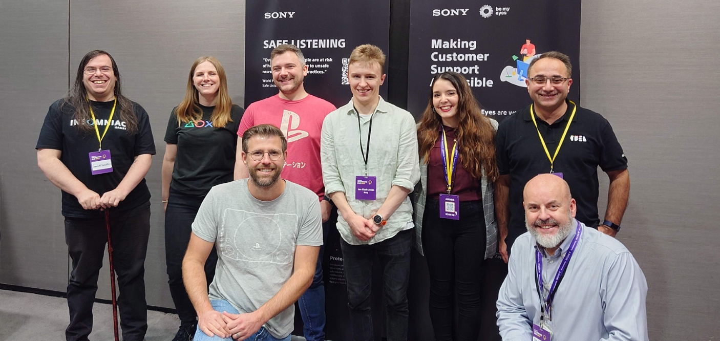 参加者が8名が展示ブースを背景に笑顔でこちらをみている。