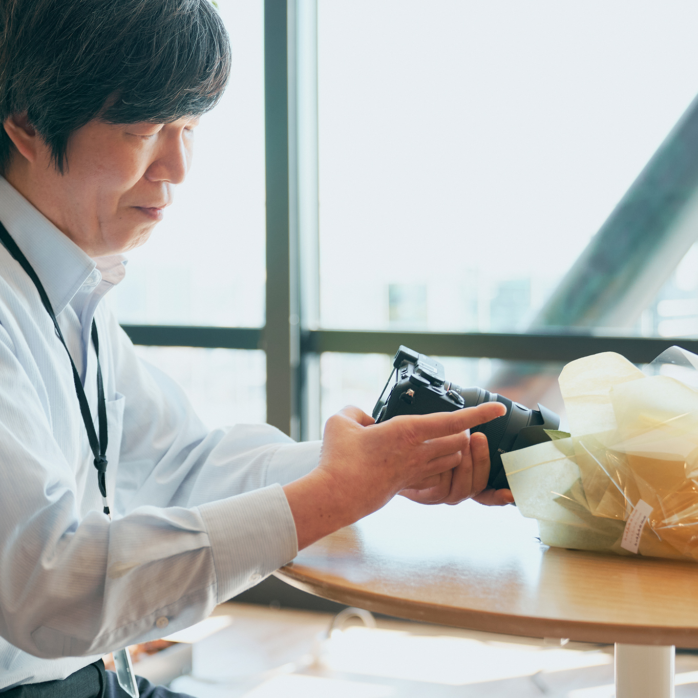 男性が窓際でカメラを持ってカメラの背面にある液晶をのみている。
