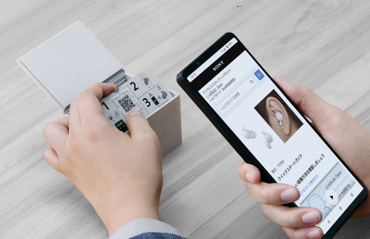 左手でソニーのLinkBuds Openのパッケージ内のGuide for QRに触れ、右手のスマートフォンでQRコードをスキャンしている写真。