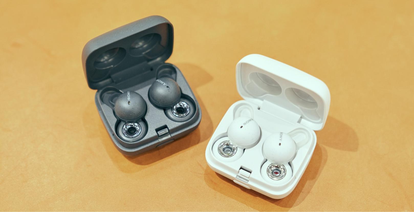 Black LinkBuds and white LinkBuds, both of which lids are open, are placed on a brown surface side by side