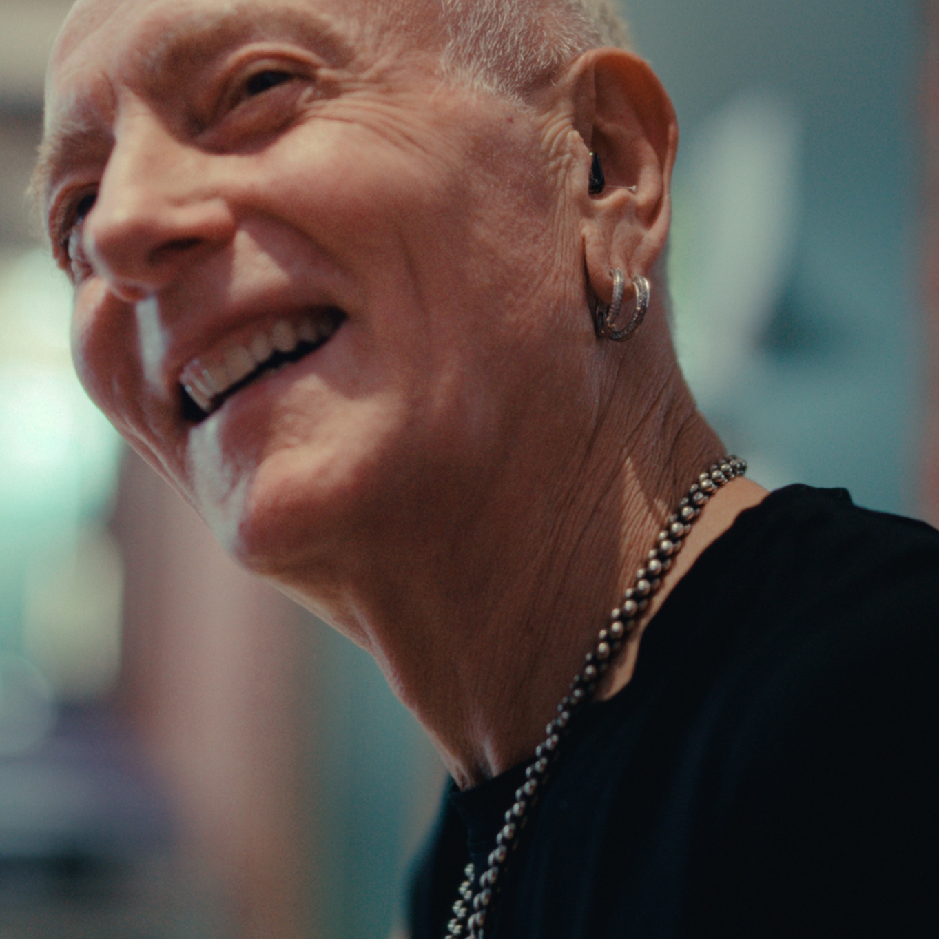 Semi-frontal portrait of musician Phil Collen with necklace and earrings, smiling