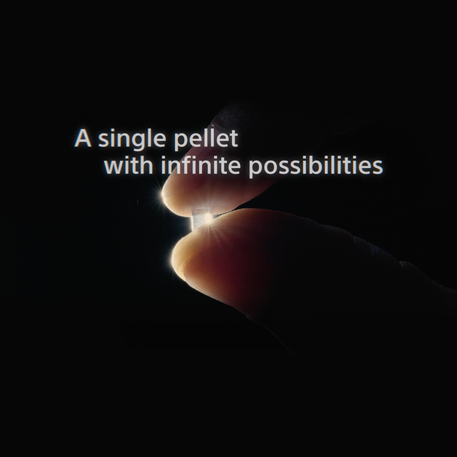 A close-up of a Sorplas pellet being picked up by the fingers. The pellet has a halo around it.